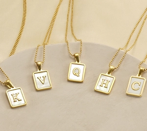 Detail of square 18K gold plated pendants with white shell and metal letters K V Q H C