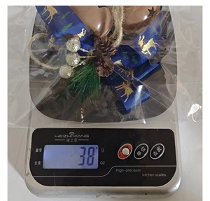 Close-up of Christmas bell ornament with pine needles and pinecones being weighed on a scale