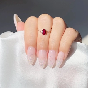 Close-up of gold chain ring featuring an oval red zircon on white satin background