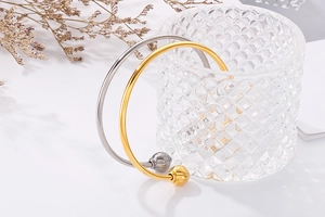 Detailed view of gold and silver minimalist open bangles with sphere ends on glass