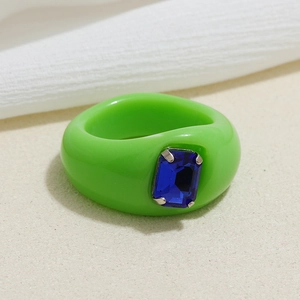 Green acrylic resin ring with square blue gemstone on a neutral textured background