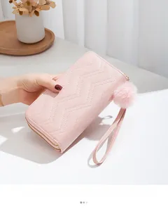 Detailed view of pink quilted long wallet with golden zippers and soft fur pompom charm