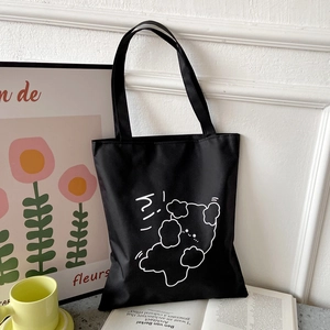 Detail shot of a black canvas tote bag featuring a cute white bear print and hi text
