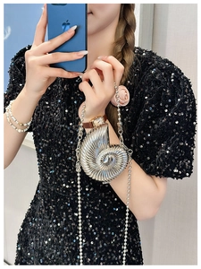 Detail of silver shell-shaped mini metal clutch bag with beaded chain on black dress