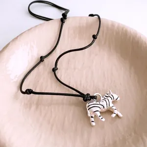 Zebra pendant necklace with black cord on ceramic tray, stylish jewelry for women