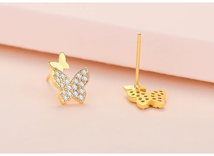 Macro view of gold butterfly stud earrings with white zirconia stones and polished finish