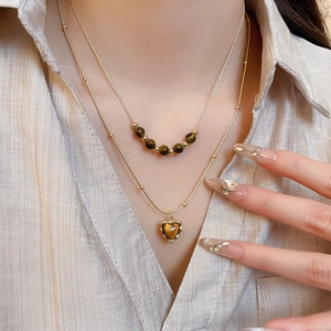 Close-up of a double-layered gold necklace with tiger eye beads and heart pendant