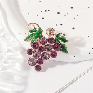 Sparkling purple crystal grape brooch with green enamel leaves on a white ceramic plate