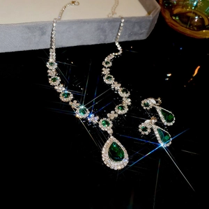 Macro shot of silver diamond necklace and waterdrop emerald earrings set on velvet box