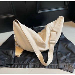 Detail showing cream nylon crescent bag texture and hardware against a black jacket