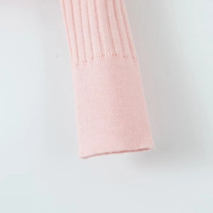 Détail de la maille côtelée verticale et du poignet sur ce pull en tricot rose doux