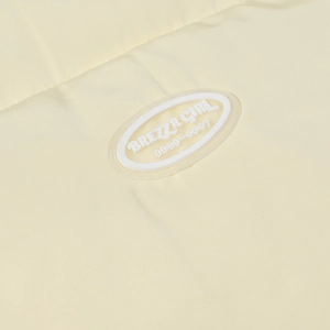 Macro shot of BREZZR GIRL rubber brand logo on creamy yellow cotton padded jacket fabric