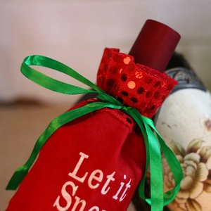 Detail of red velvet wine gift bag with green silk ribbon and Let it Snow embroidery