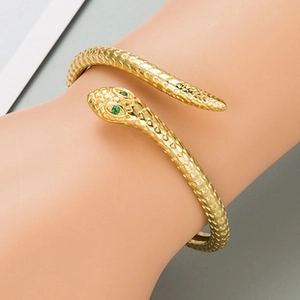 Detail of a golden snake bracelet featuring green gemstone eyes and scales on the wrist