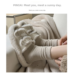 Detail of beige plush buckle slippers paired with thick grey knitted socks on soft sofa