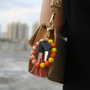 Silicone bead keychain with orange tassel attached to a beige handbag on city background