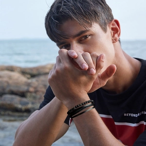 Detail of male model wearing multi-layered black bead and braided leather bracelets on beach