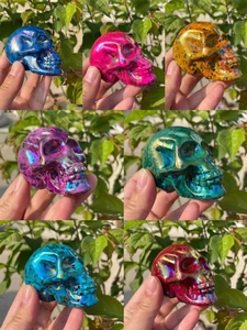 Macro shot of 7cm aura crystal skulls in various colors held against greenery