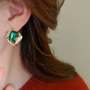 Close-up of vintage golden geometric earrings with emerald green square crystal on model