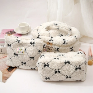 Detailed view of three white lamb wool makeup bags featuring black bows and quilted patterns