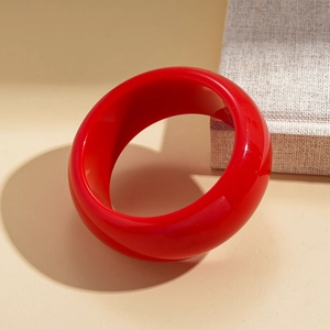 Close-up of a wide red resin bangle with glossy finish on a minimalist background
