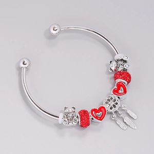 Silver bead bracelet with red heart, bear charm, and feather pendant on light background