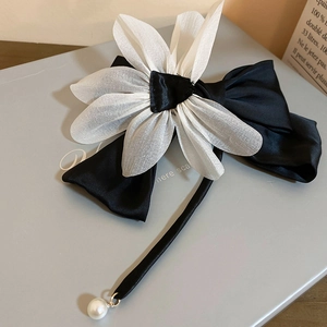 Detail of elegant black ribbon bow clip featuring a white 3D flower and a pearl drop charm