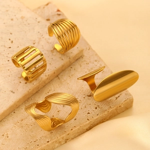 Detailed view of four golden geometric stainless steel rings on a beige travertine surface