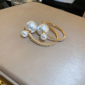 Macro detail of gold C-shape hoop earrings with faux pearls and sparkling rhinestones