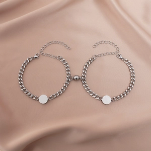 Close-up of silver Cuban link couple bracelets with magnetic charms on silk