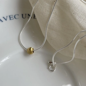 Detail of silver snake chain necklace with a brushed gold bead on a ceramic plate