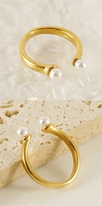 Detail of an adjustable gold open ring featuring elegant double pearls on a stone surface