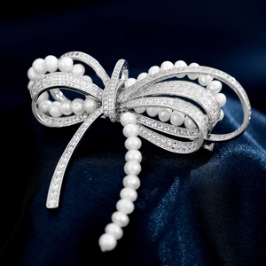 Macro detail of silver bow brooch with pavé zircon stones and white pearls on silk