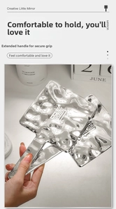 Detail of silver handheld makeup mirror with unique ripple texture and long handle