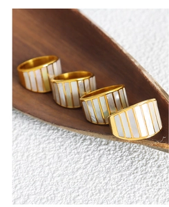Detail of gold plated rings with white shell inlays and textured vertical stripes