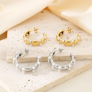 Detailed macro shot of gold and silver C-shaped pearl earrings on a stone base