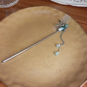 Detail of silver bamboo-style hair pin with green tassels in a rustic ceramic plate