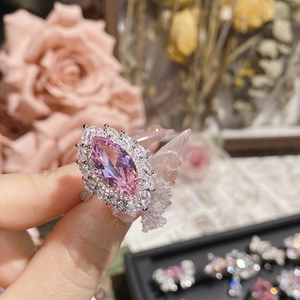 Nahaufnahme eines Rings mit rosa Markiseschliff-Kristall vor elegantem Blumenhintergrund