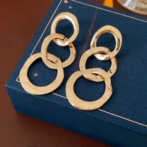 Textured gold triple-link drop earrings with hammered finish on dark jewelry box