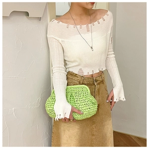 Detail of neon green woven clutch bag paired with a white distressed knit sweater