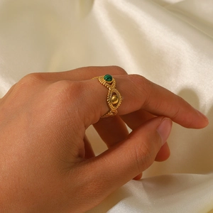 Close-up of 18K gold ring with green gemstone worn on hand over beige silk background