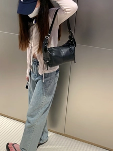 Close-up of minimalist black leather shoulder bag with smooth zipper detail on model