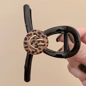 Elegant black claw clip with leopard print disc and gold smiley face held in hand