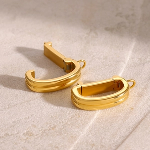 Detailed view of polished golden U-shaped hinge earrings on textured stone surface