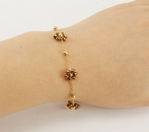 Close-up of a gold chain bracelet with brown beaded flowers on a model's wrist