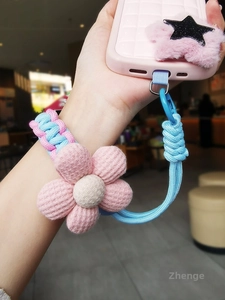 Close-up of a pink woven wrist strap with a floral charm and pink star phone case