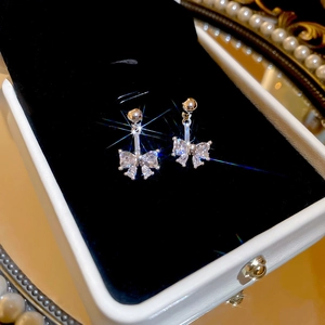 Macro shot of silver bow earrings with zircon stones on a black velvet jewelry box cushion