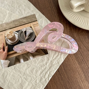Close-up of a large pink holographic heart hair claw clip on a lifestyle background