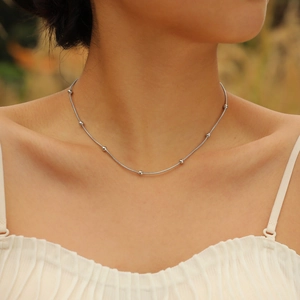 Close-up of a minimalist silver beaded snake chain necklace worn on a woman's collarbone
