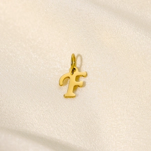 Detail of a golden letter F pendant with a round clasp on elegant beige silk fabric